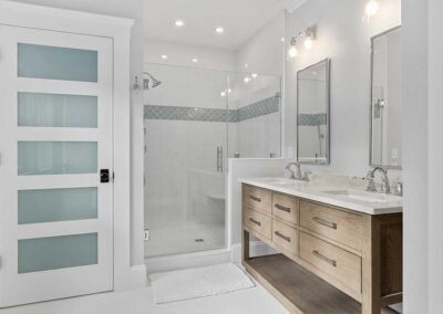 Bathroom with two sinks and a walk in shower with a bench